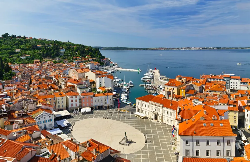 Ovalformade Tartini-torget, gamla stenhus, smala gator, hamn och små båtar i Piran, Slovenien.
